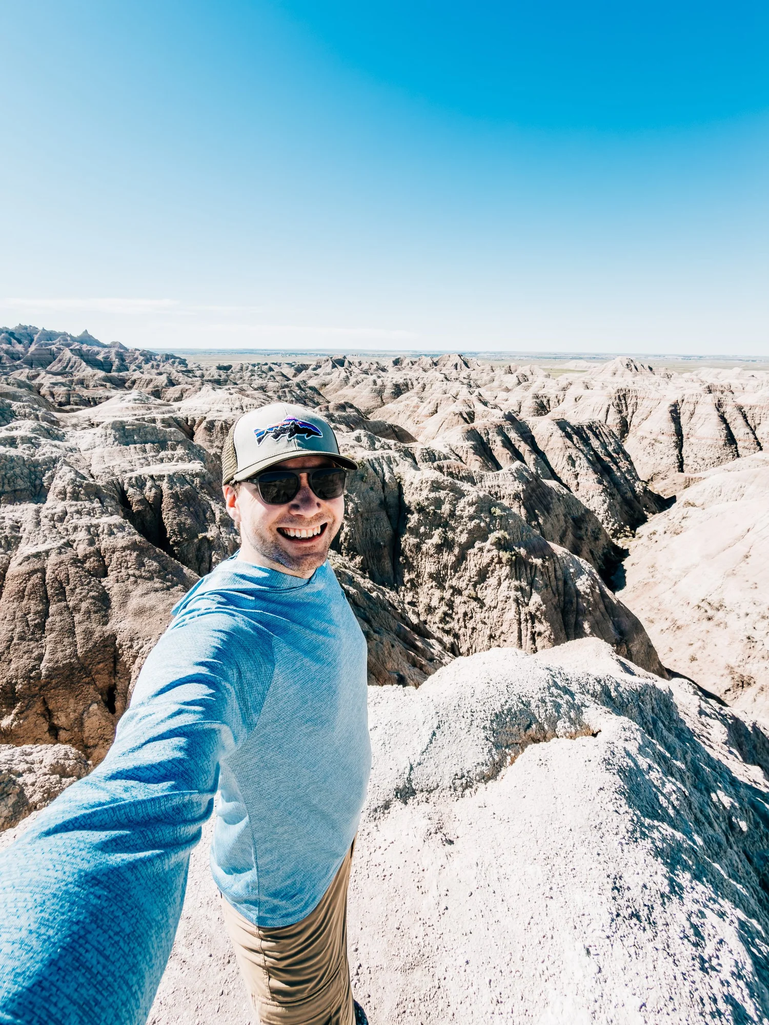 Smiling selfie on a rocky Badlands overlook with eroded ridges stretching to the horizon under a deep blue sky