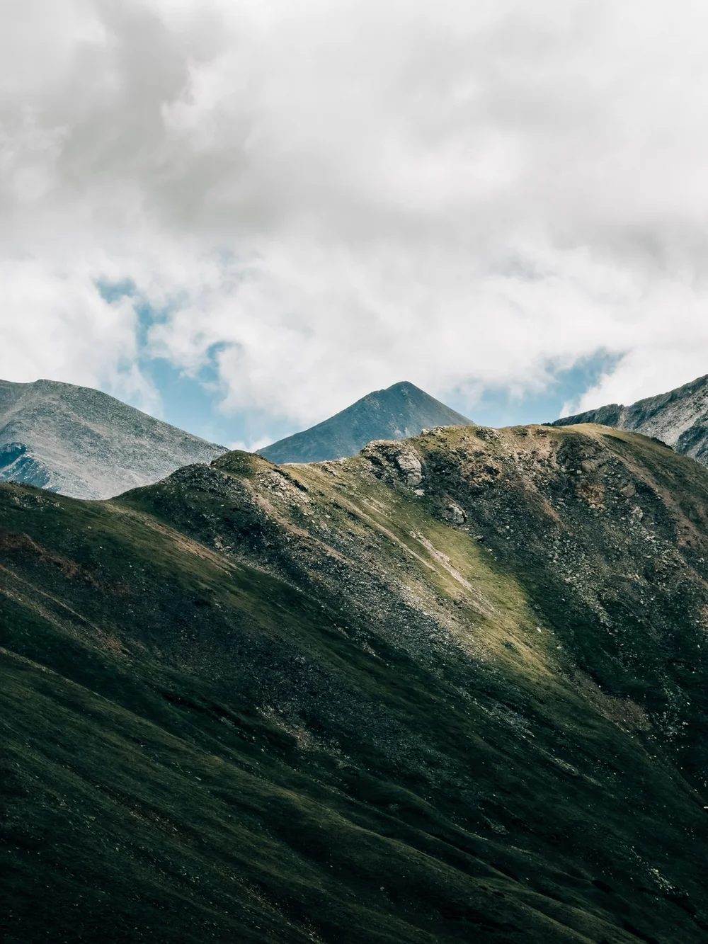 Grays and Torreys peaks rising behind a sunlit green ridge under heavy clouds