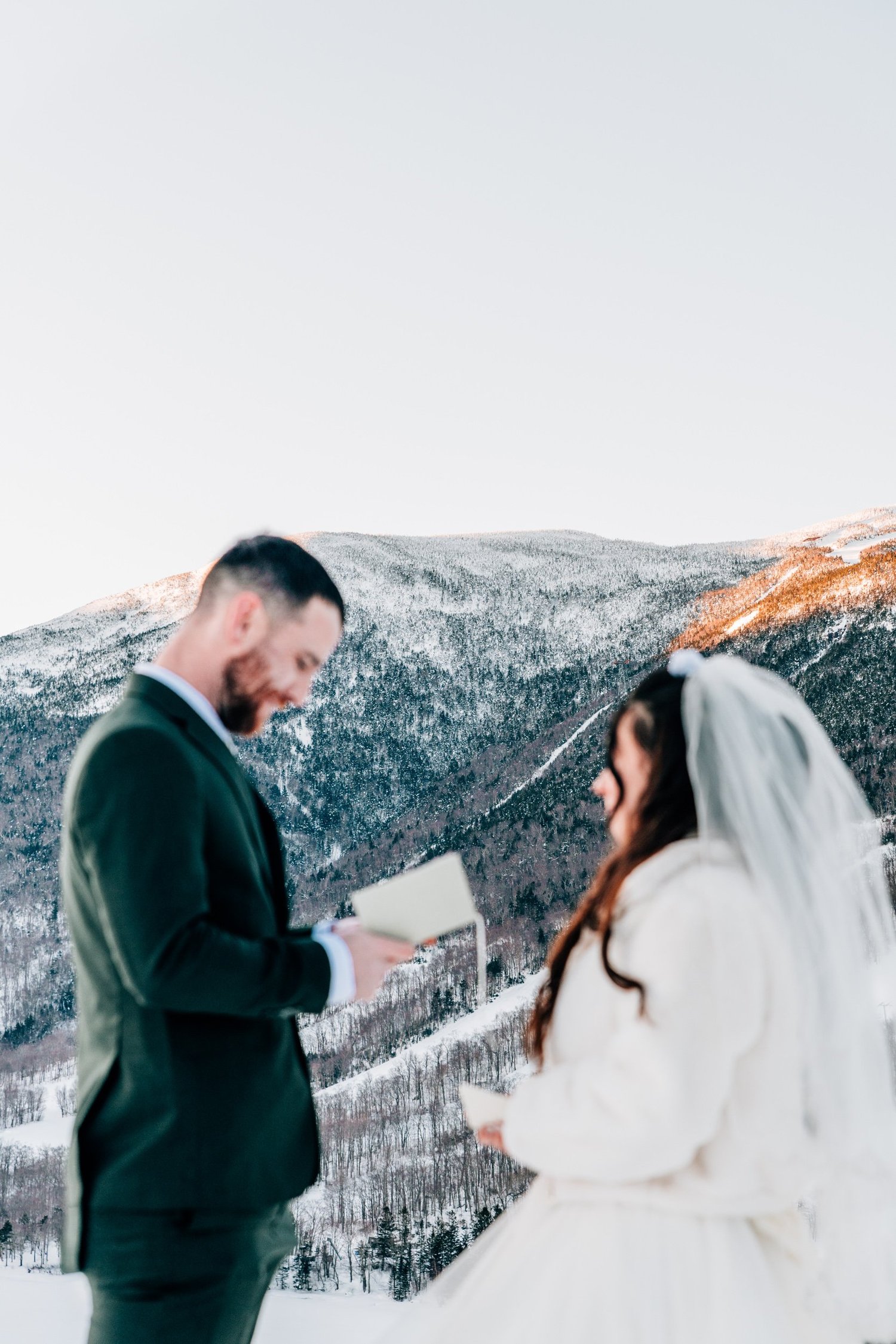 Groom reading his vows to his bride with snowy mountains behind them in New Hampshire