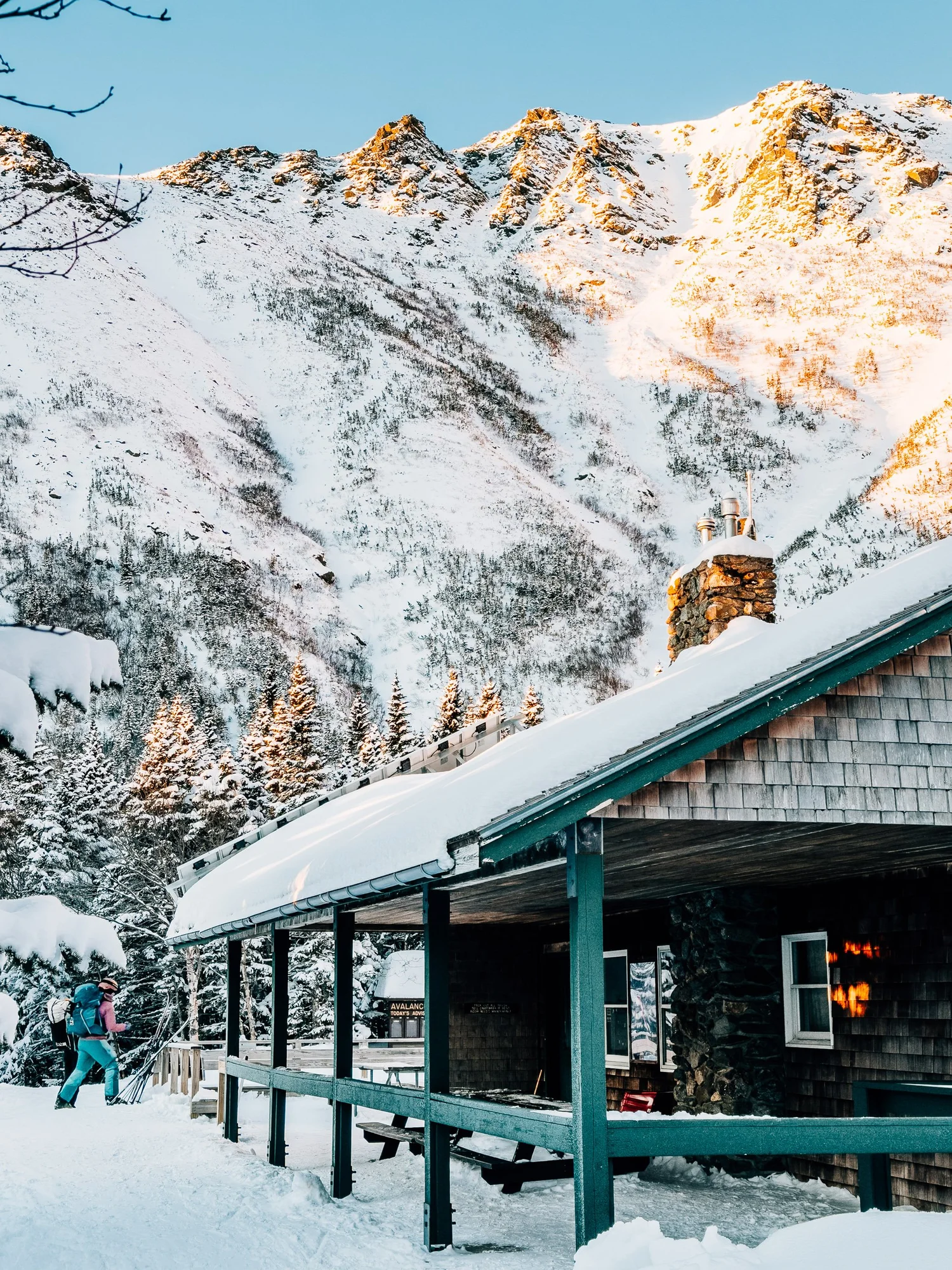 Snow-covered cabin below Tuckerman Ravine in winter, with sunrise light on the headwall above