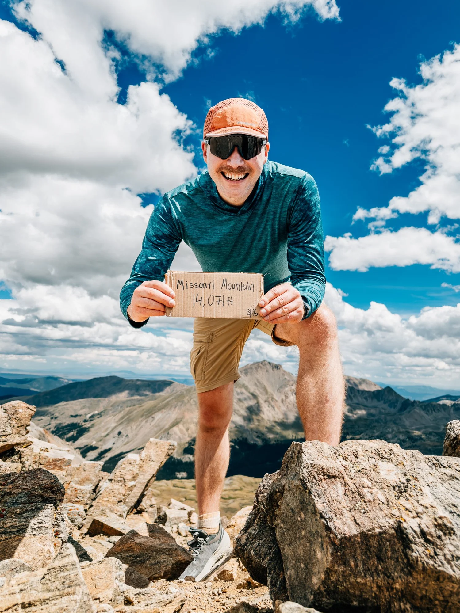 Anton on the Missouri Mountain summit holding a cardboard sign reading 14,071 ft, Collegiate Peaks behind