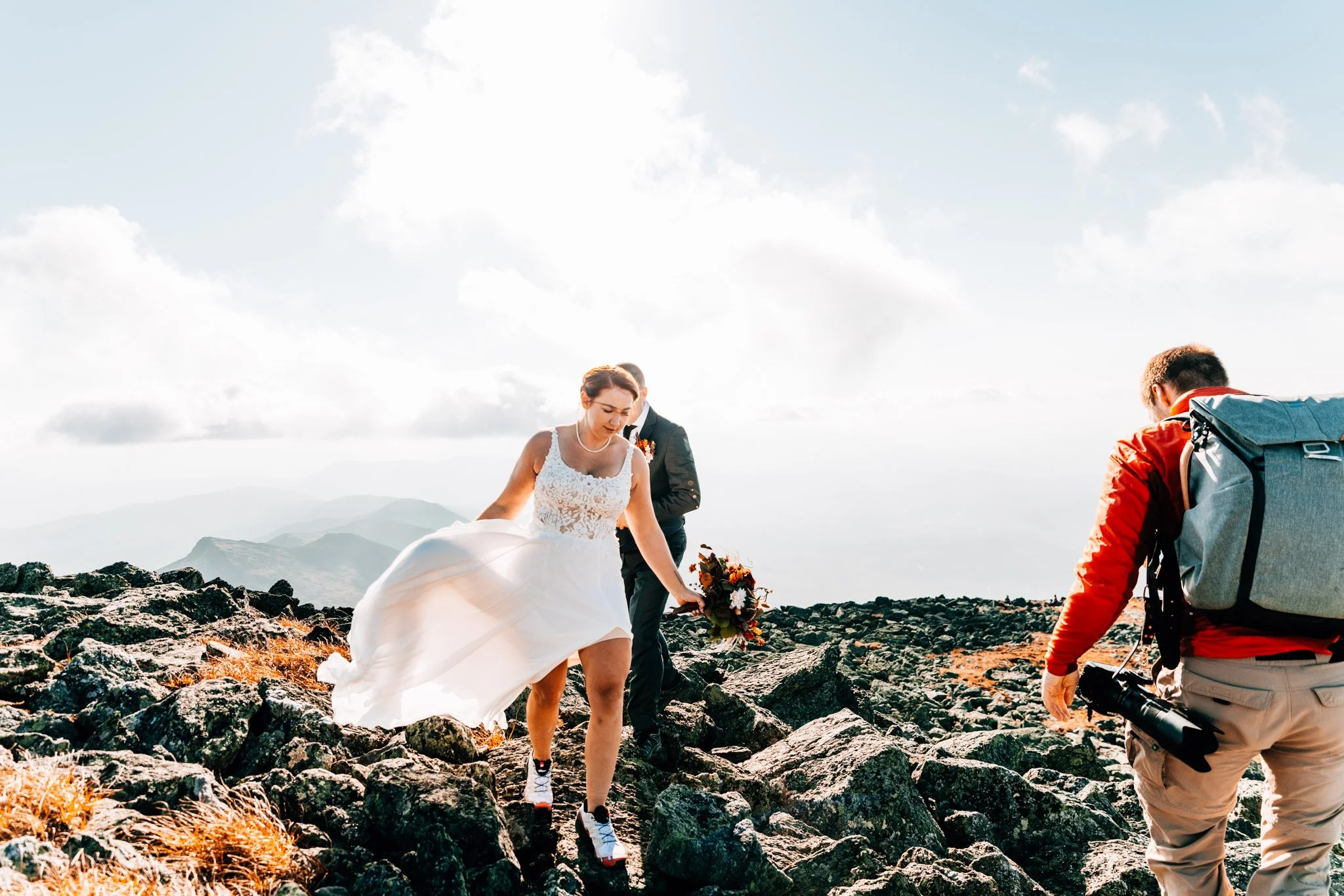 Couple picking their way across a rocky alpine summit with a photographer following