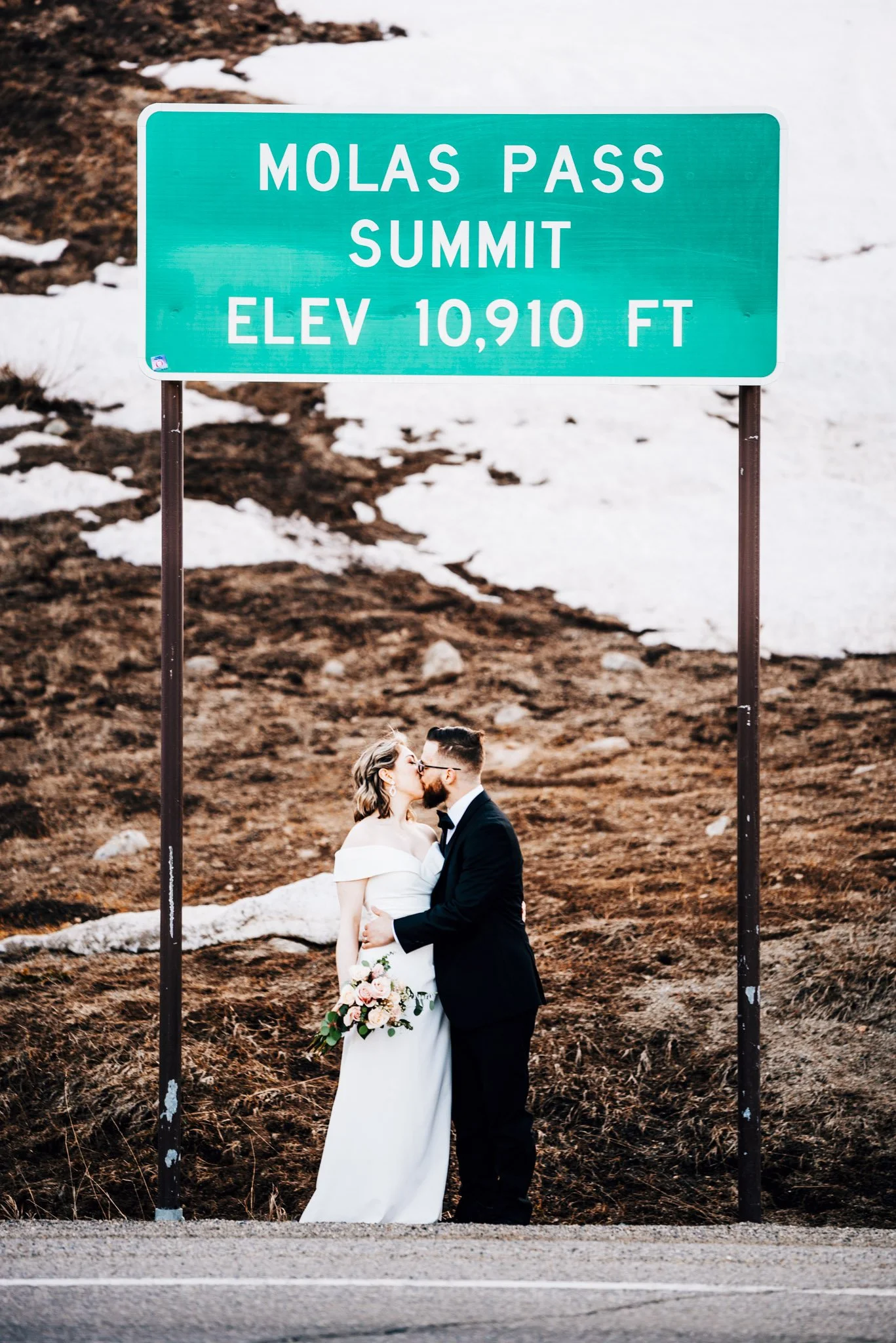 Couple kissing beneath the Molas Pass summit elevation sign in Colorado