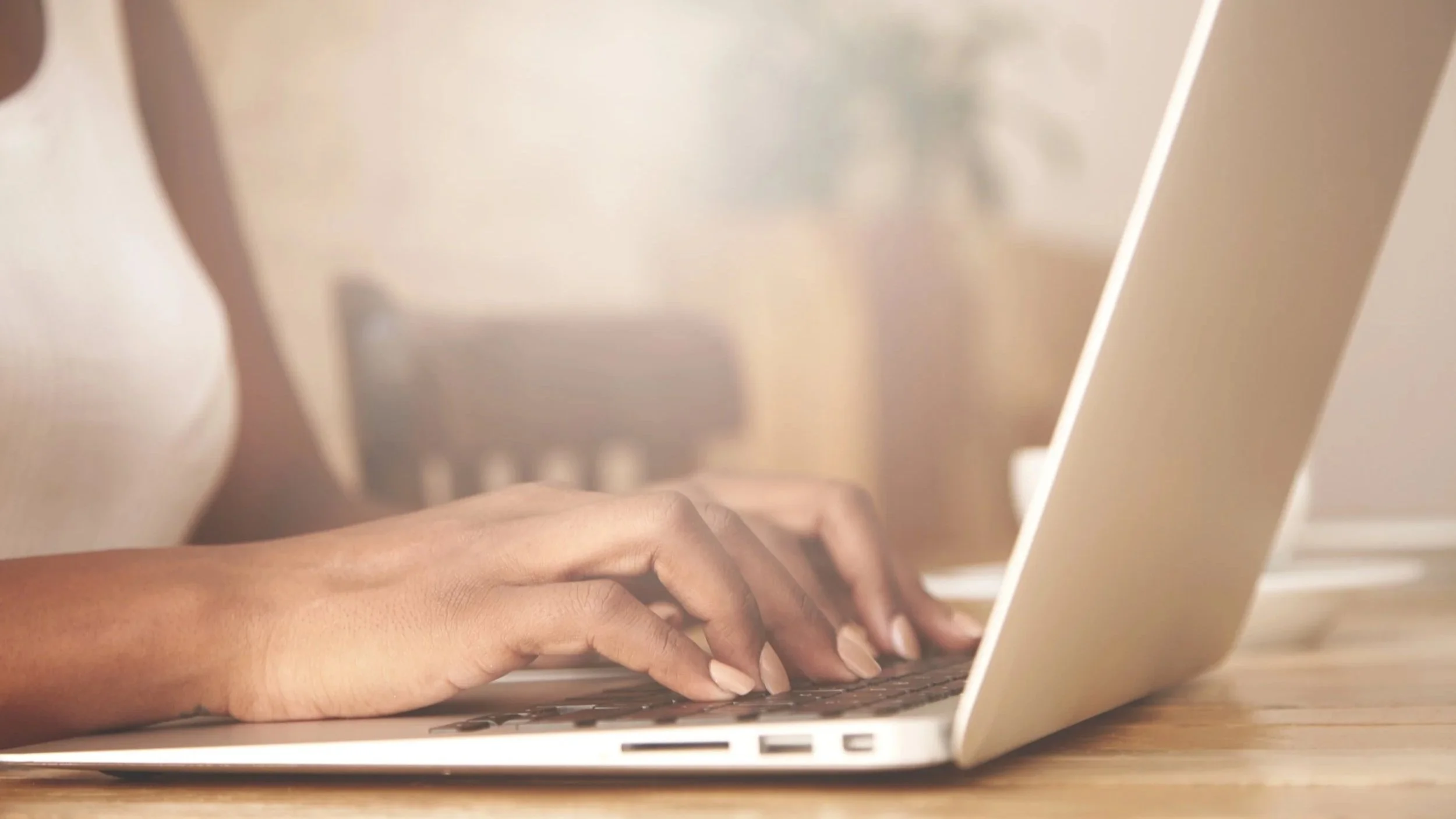 Close-up of a person's hand typing on a silver laptop keyboard on a wooden surface.