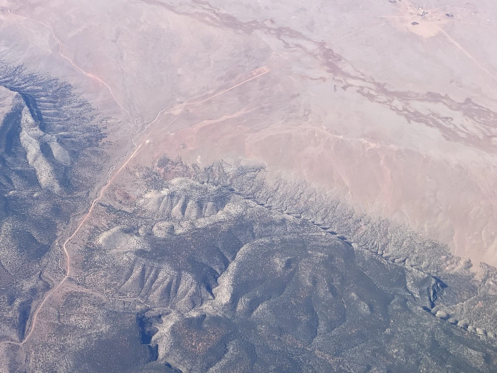Aerial view of a desert landscape with mountains, valleys, and a sparse road cutting through the terrain.