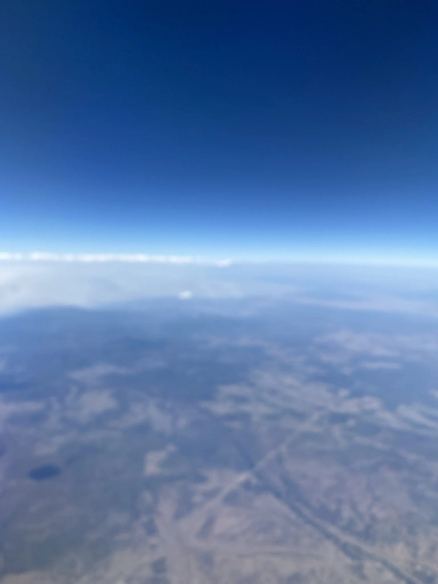 A view from high altitude in the sky showing the blue sky above a layer of clouds and the Earth's surface below.