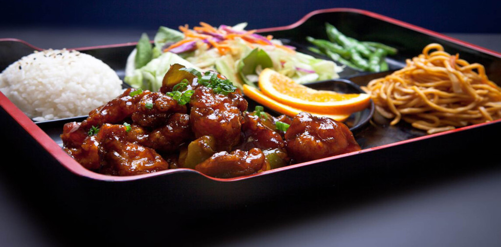 A Bento box is served with a meat entree, white rice, lo mein noodles, string beans, and a ginger salad.