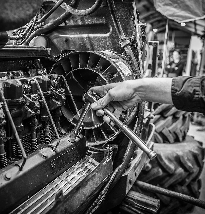 A person is repairing or inspecting a large engine using a wrench in an industrial or workshop setting. This is a photo by one of the top hawkes bay wedding photographers, Eva Bradley