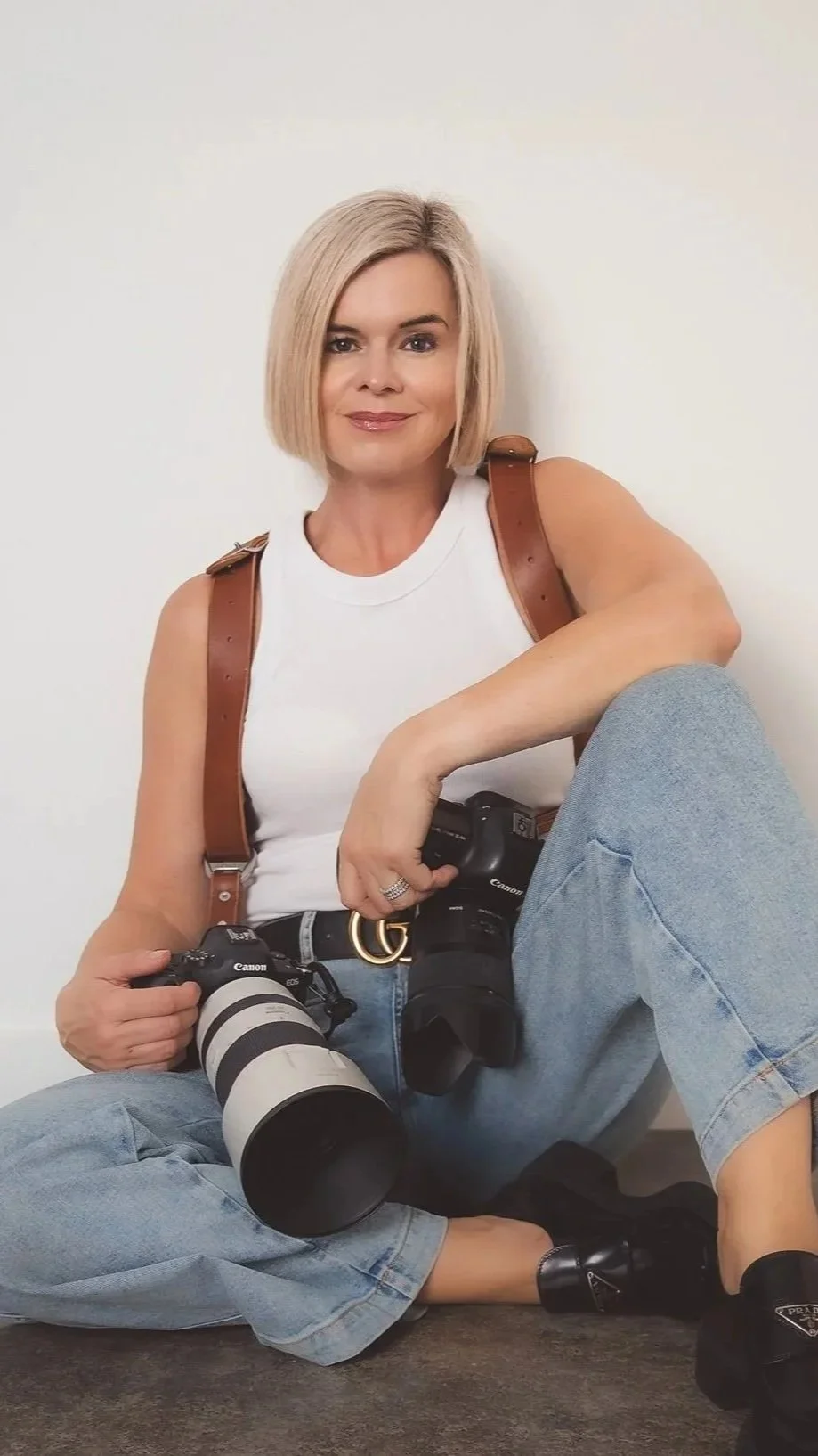 A photo of Eva Bradley, the top wedding photographer in Hawkes Bay, sitting on the ground holding her cameras. These are her prices for wedding photography