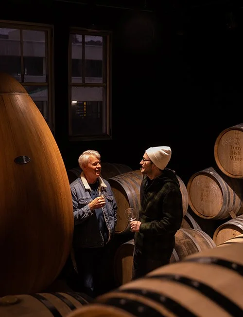 Two men inside a winery talk and have a glass of wine in a photo by one of the best commercial photographers in Hawke's Bay, Eva Bradley, from Napier