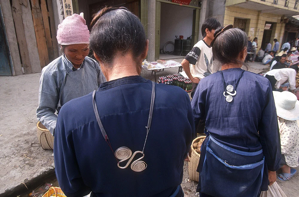 Mulheres Dong com roupas tradicionais tingidas de índigo. As peças em prata que se veem nas suas costas são utilizadas como contra-peso para uma espécie de avental.
