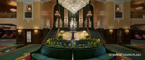 Interior of a luxurious hotel lobby with a grand chandelier, a fountain in the center, surrounding greenery, and stairs leading to upper floors.