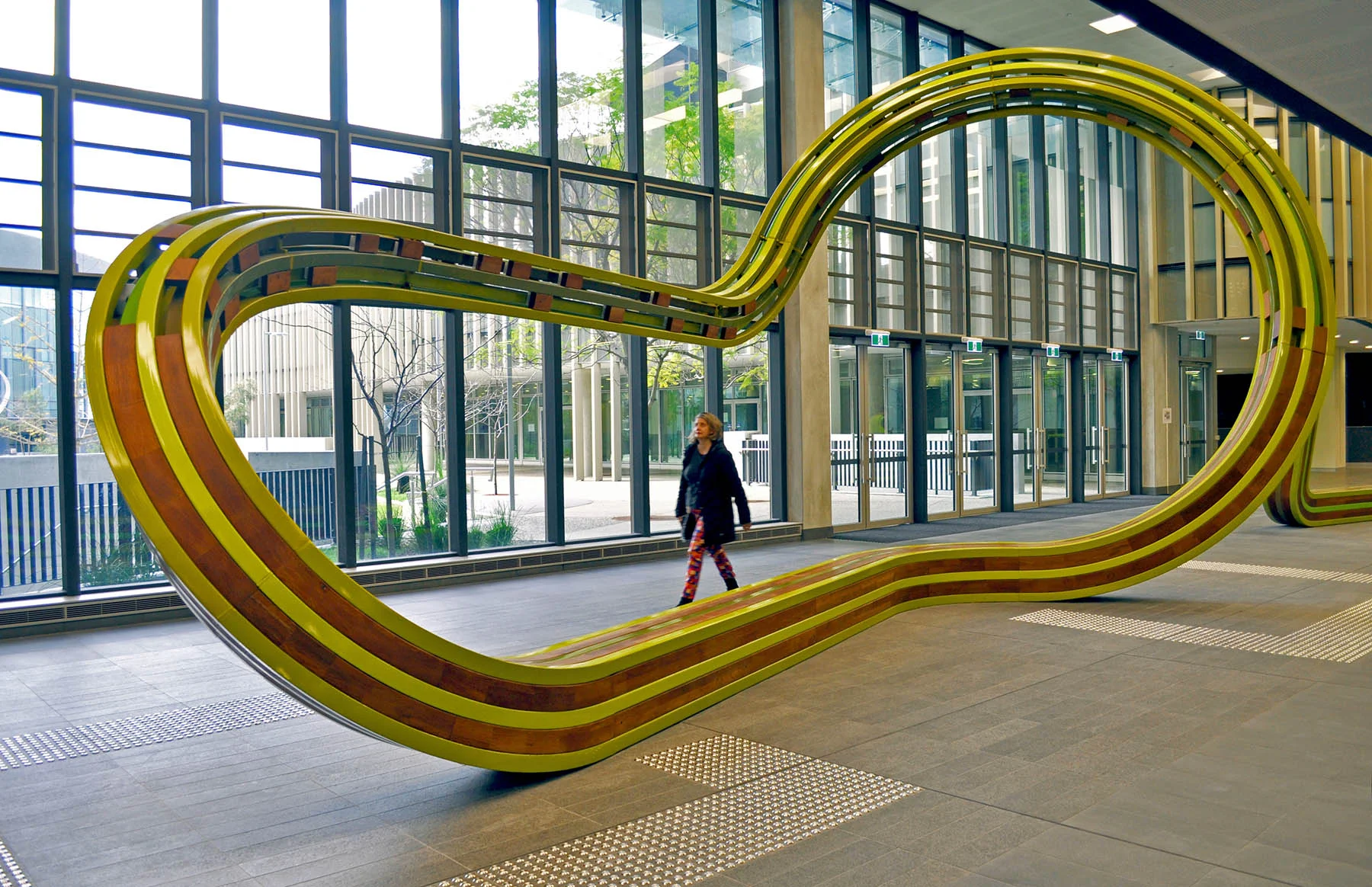 In between and all around is designed to be a continuous loop of steel and timber running overhead and defying gravity. As a major public artwork for the Perth facility, it creates the central way-finding attraction for the newly built Fiona Stanley Hospital. Two complementary public artwork pieces are placed adjacent to the large loop. Reminiscent of felled tree trunks, these artworks act both as a visual link to, and extending the main work, as well as providing practical seating.