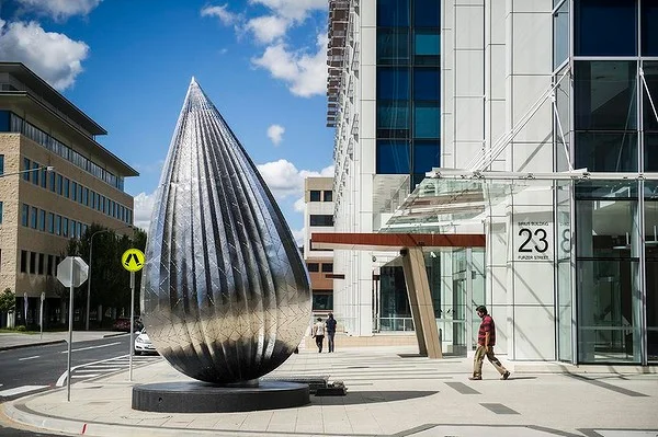 The jewel-like Droplet sits at an angle to reinforce its precarious and weighty presence. Droplet is made of stainless steel pleats, each pierced to create a highly decorative, reflective and mesmeric surface pattern. Powerful internal LED lights illuminate the Public artworkfrom within and at night, give the sculpture a sense of transparency and weightlessness that contrasts with its daytime mass.