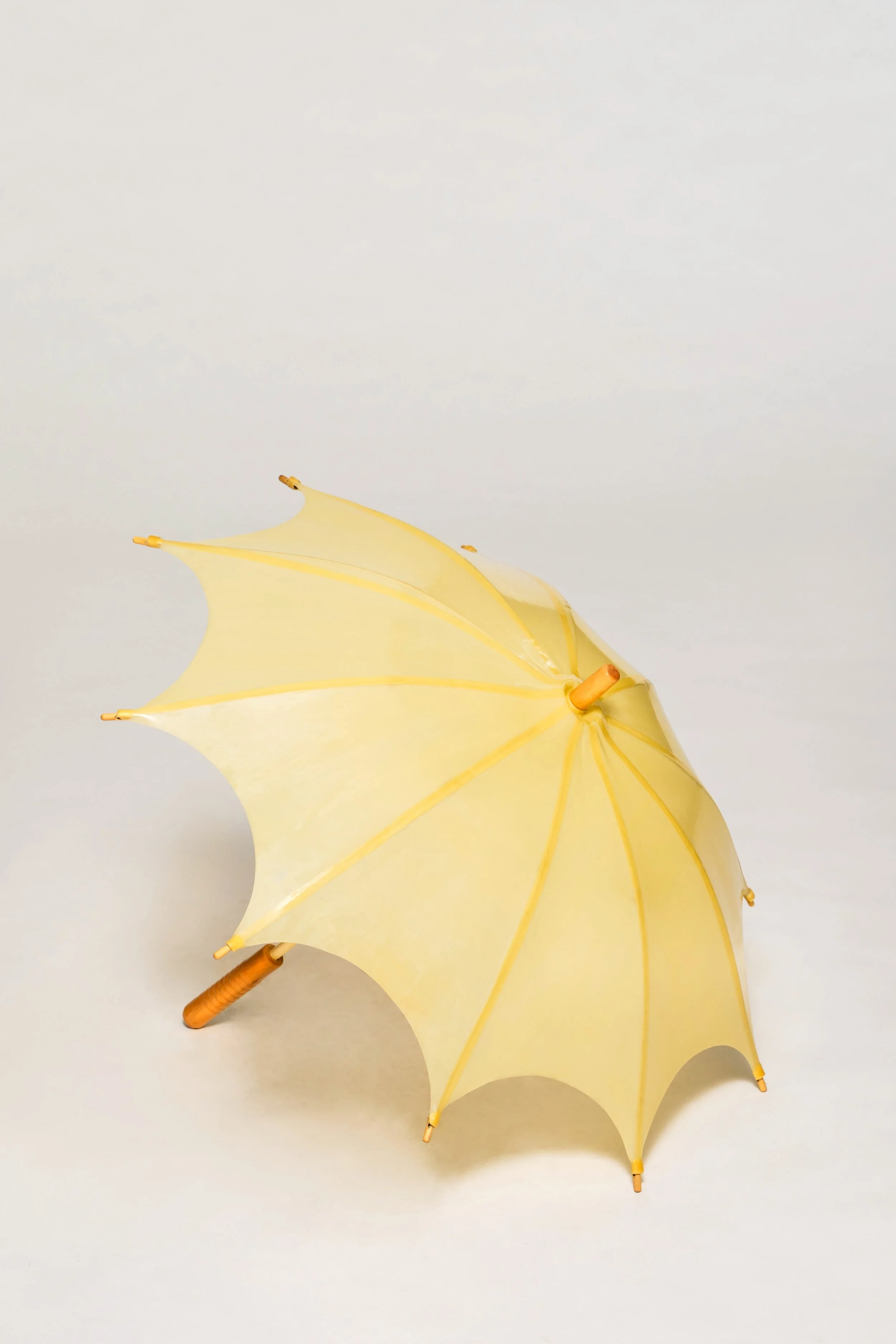 Yellow natural latex umbrella with wooden shaft and curved sculptural canopy panels on neutral background.