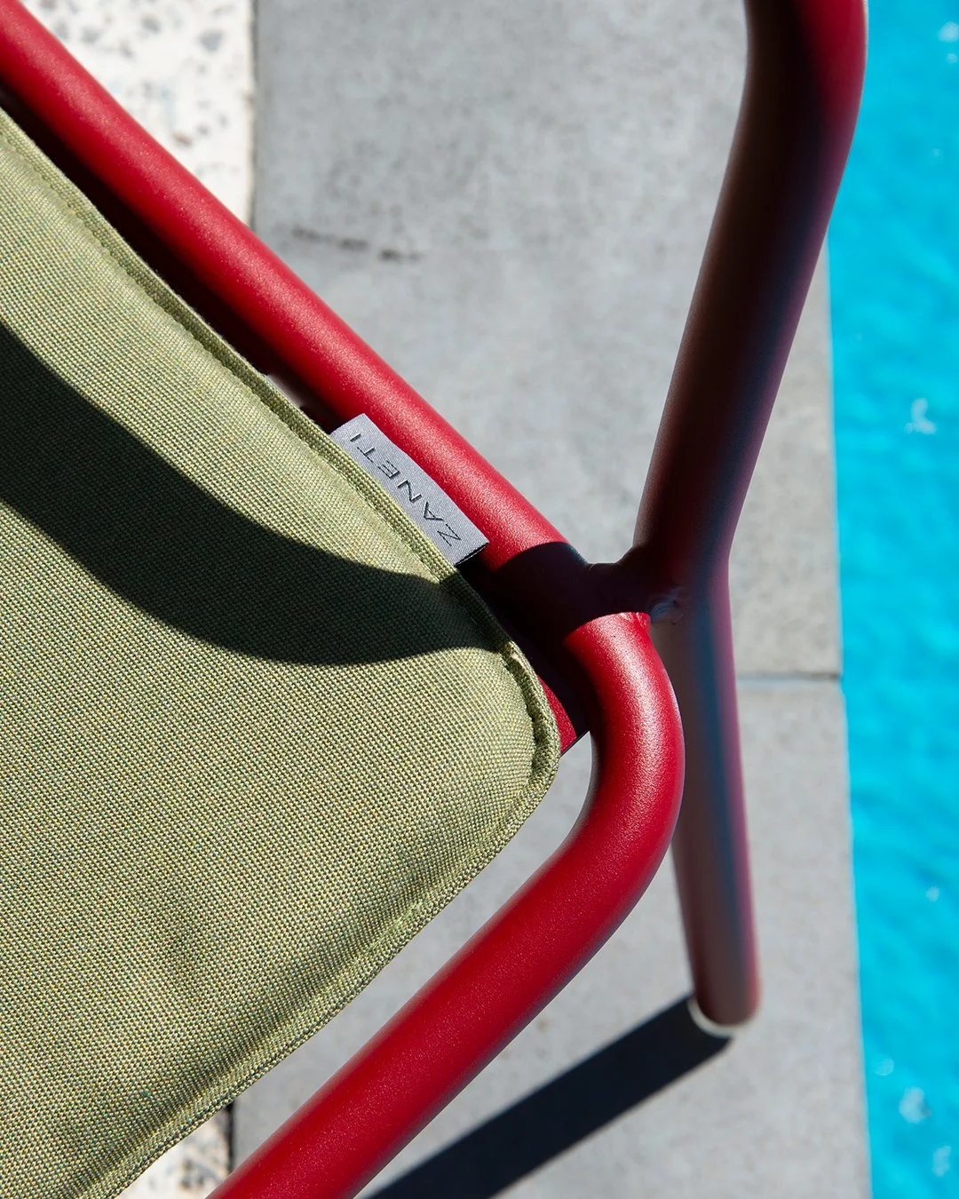 Close-up of a green fabric lounge chair with a red metal frame next to a swimming pool.
