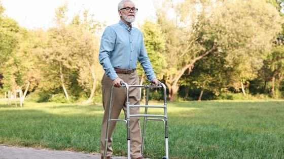 old man walking with walker in park indicating inevitable disability.