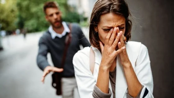 crying woman walking away from a man who is trying to talk.