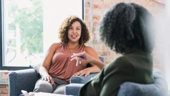 black woman looking relaxed with her black woman therapist relating over shared stories and self-disclosures.