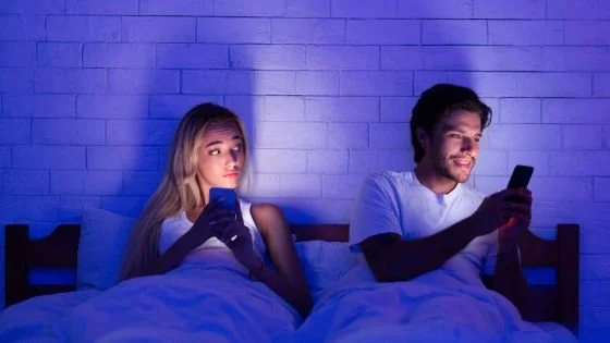 couple in bed together both on their phones; woman looking suspicious at man's activity. This indicates talking openly about social media preferences.