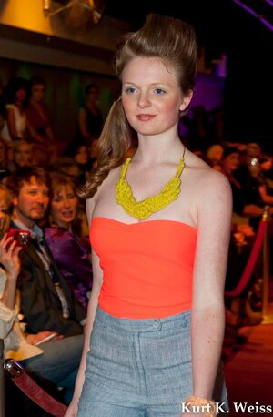 A model walks runway in a neon orange strapless top and high waisted denim shorts made by Alaina Smith