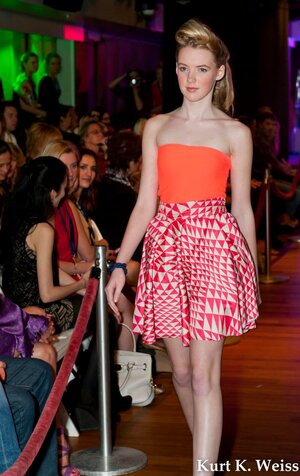 Model walks runway wearing neon orange strapless top and graphic geometric print orange skirt