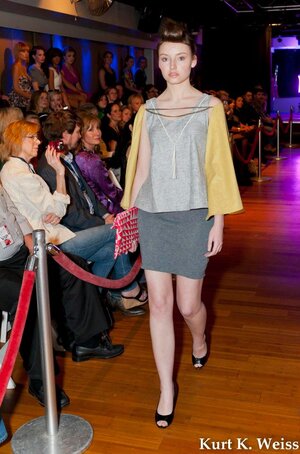 Model walks Knoxville Fashion Week 2016 Runway in a gray pencil skirt, flowing gray top, and gold capelet. 