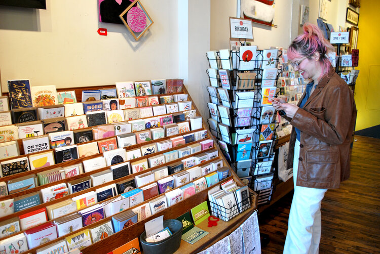 Shelby of Cold Gold laughs at a birthday card next to a card display in Rala 
