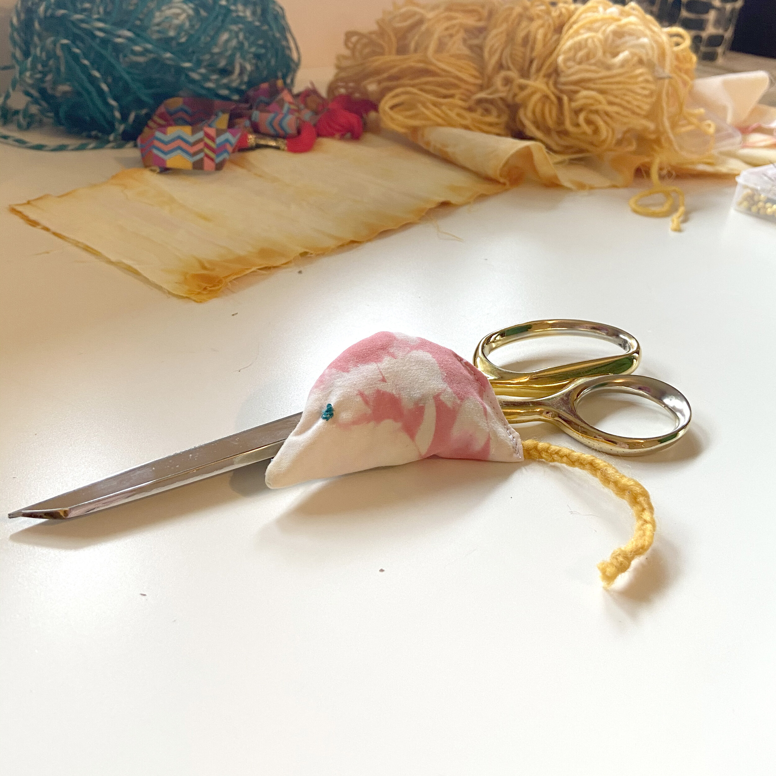 Completed mouse shaped cat toy made of tie dye scrap fabric displayed on table with gold scissors.