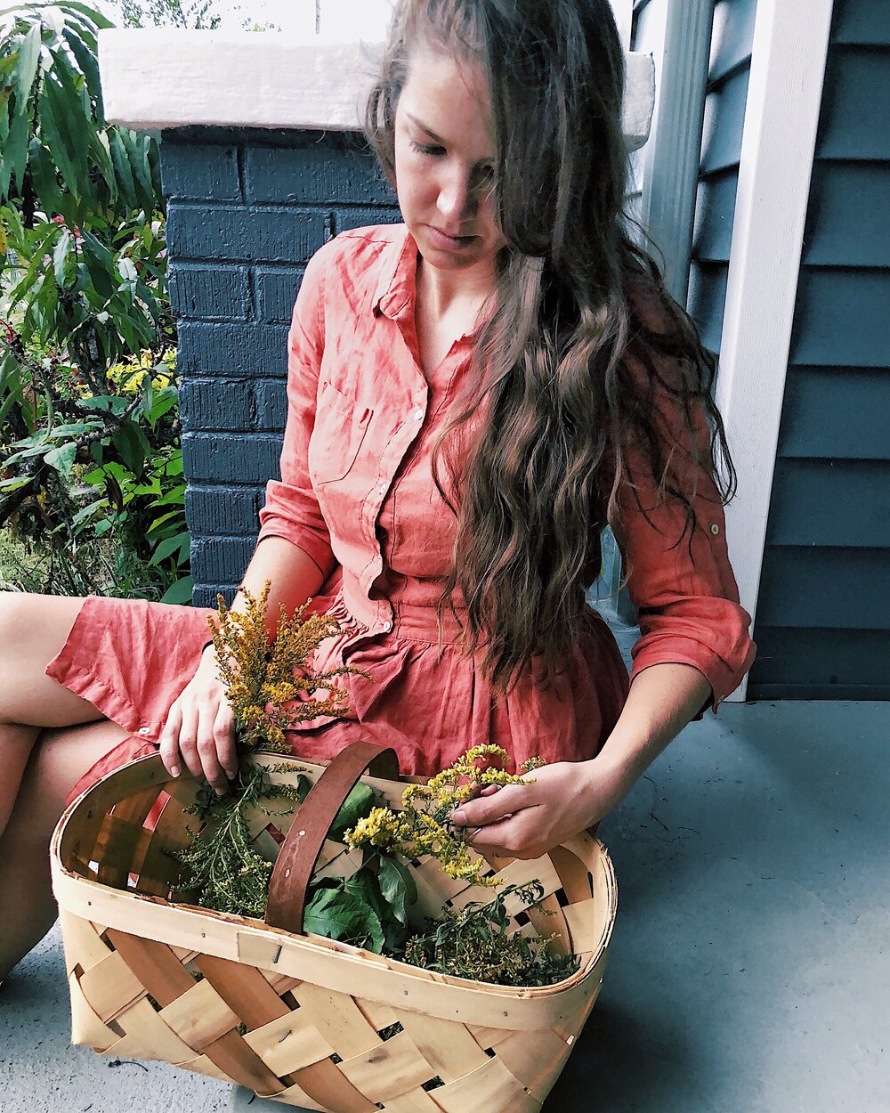 Meg Edwards owner of Flora Wellness, sits on her porch with foraged remedy ingredients in a basket.  photo credit Flora Wellness