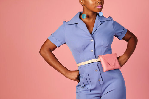 A model wears a blue jumpsuit with a bubblegum pink belt bag around her natural waist.