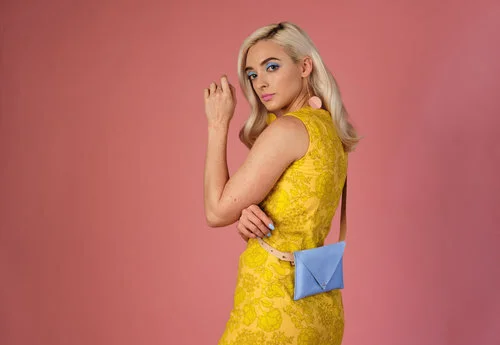 A model wears a periwinkle blue belt bag cross body style over a sleeveless yellow dress. 