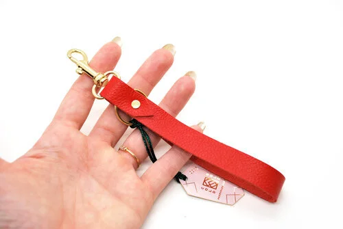 Poppy red leather key chain displayed on a hand against a white background. 