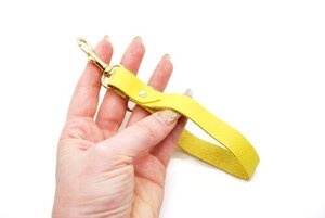 Leather yellow key chain wristlet displayed on a hand against a white background. 
