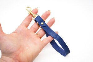 The Leather wrist strap keychain in Navy Blue displayed on a hand against a white background. 