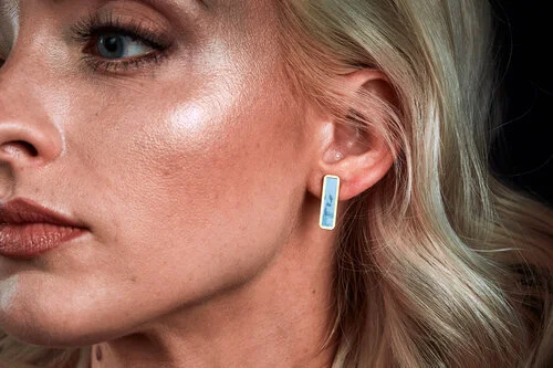 A closeup portrait of a blonde model wearing the aqua marble long bar studs. 