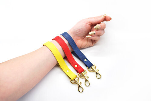 Three keychain wristlets in navy, yellow, and redon an arm against a white background. 