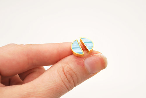 A hand holding a pair of geometric half moon studs in aqua marble. 