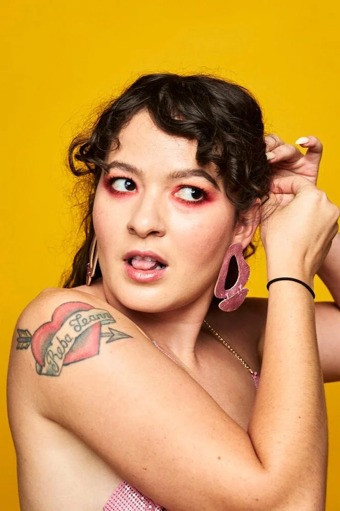 A dark haired woman wears the oversized leather Inferno Earrings in Metallic Pink.