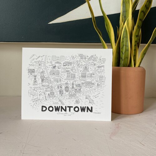 A print of Paris Woodhull’s hand drawn map of Downtown Knoxville propped against a potted snake plant. photo via ParisWoodhull.com.