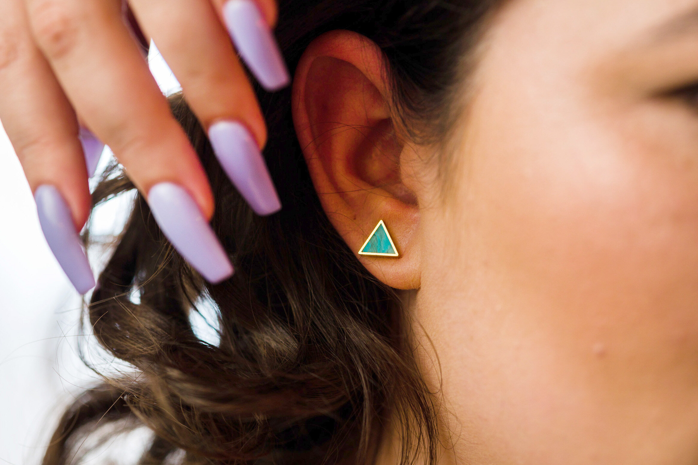 a model with long lavender fingernails wears the aquamarine triangle geo stud earrings.