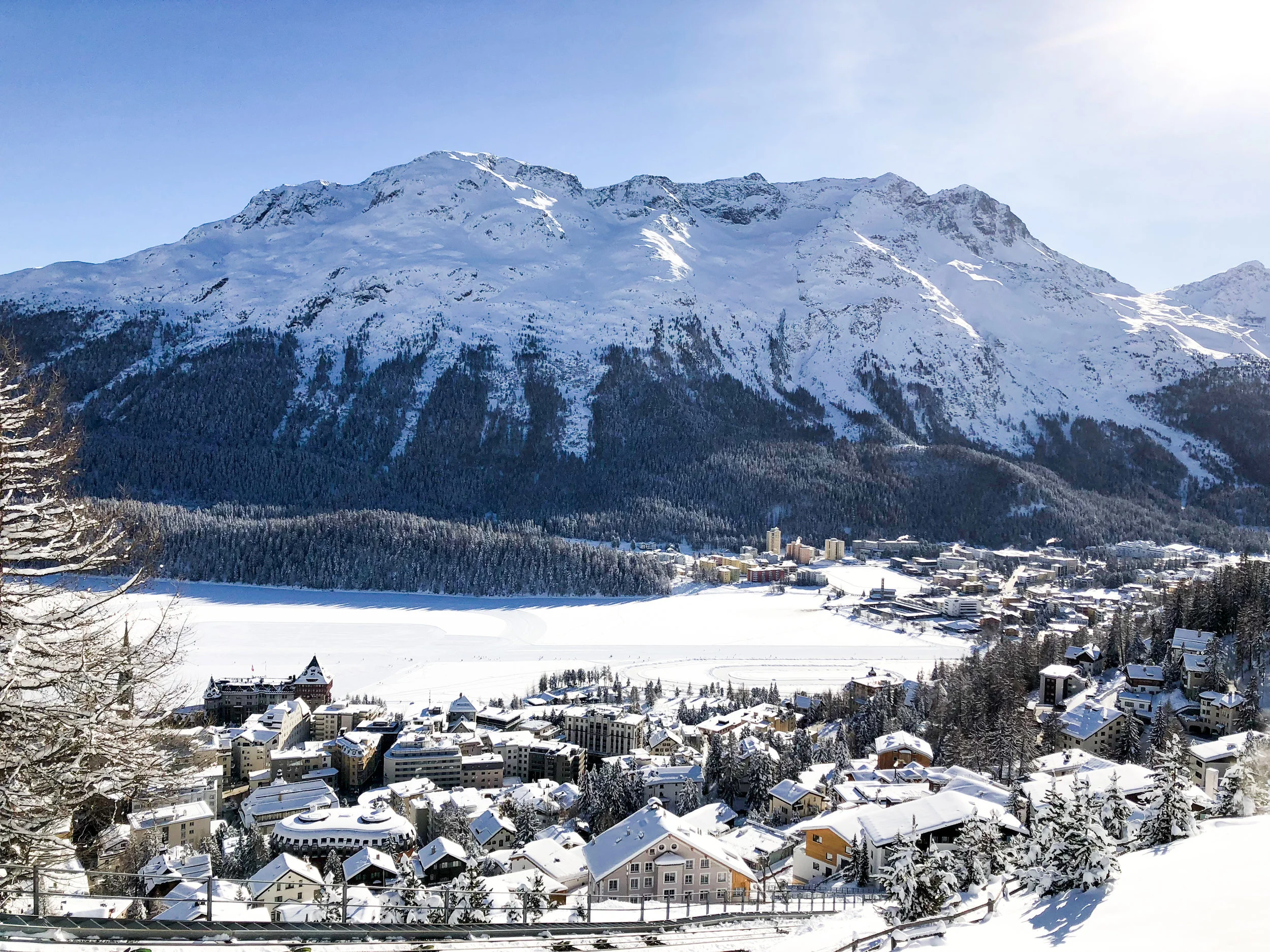 The frozen lake covered in snow with the towering mountains above the town.