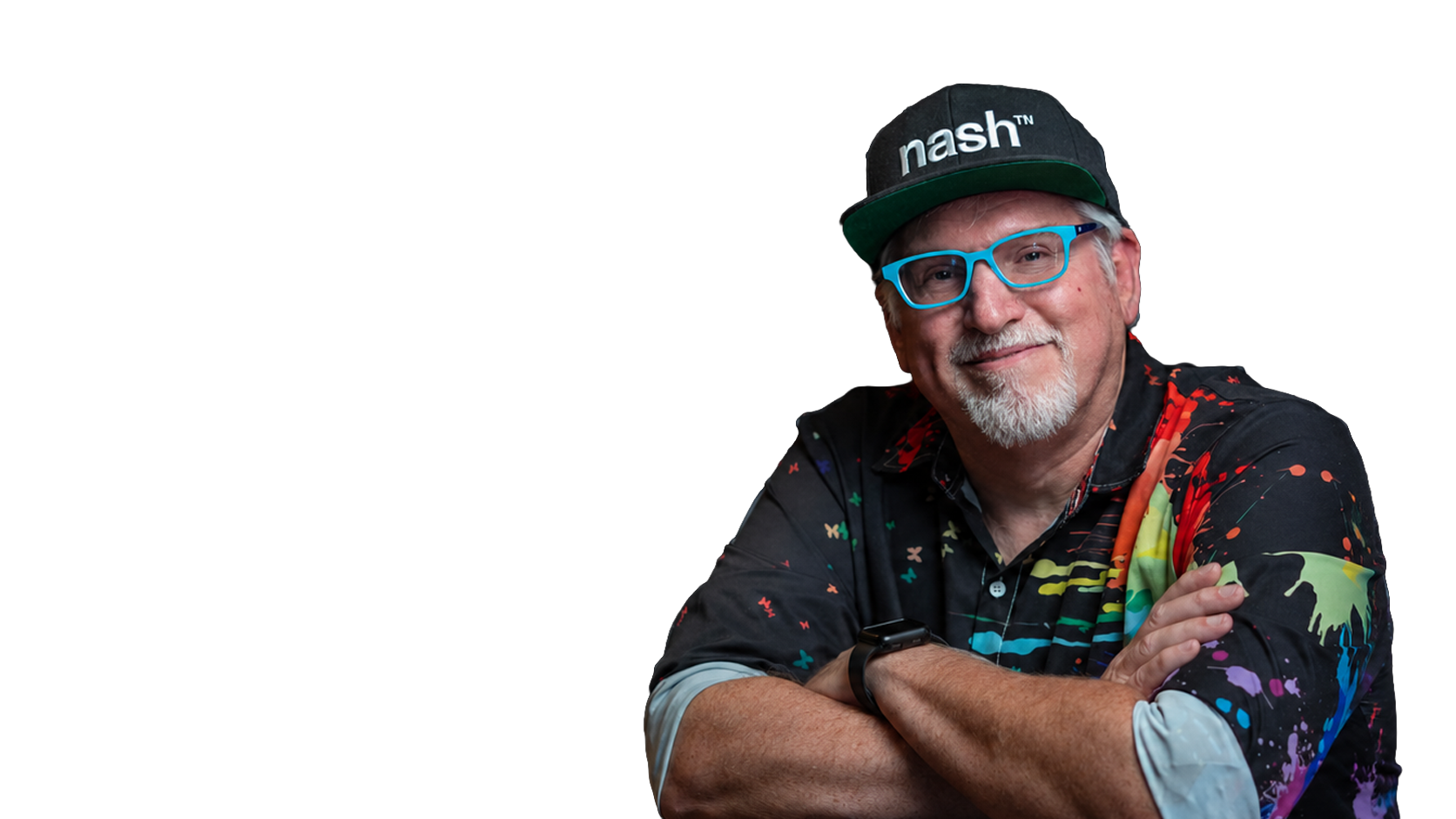 Smiling man with white beard wearing a colorful shirt, blue glasses, and a black cap with 'nash' written on it, crossing his arms against a black background.