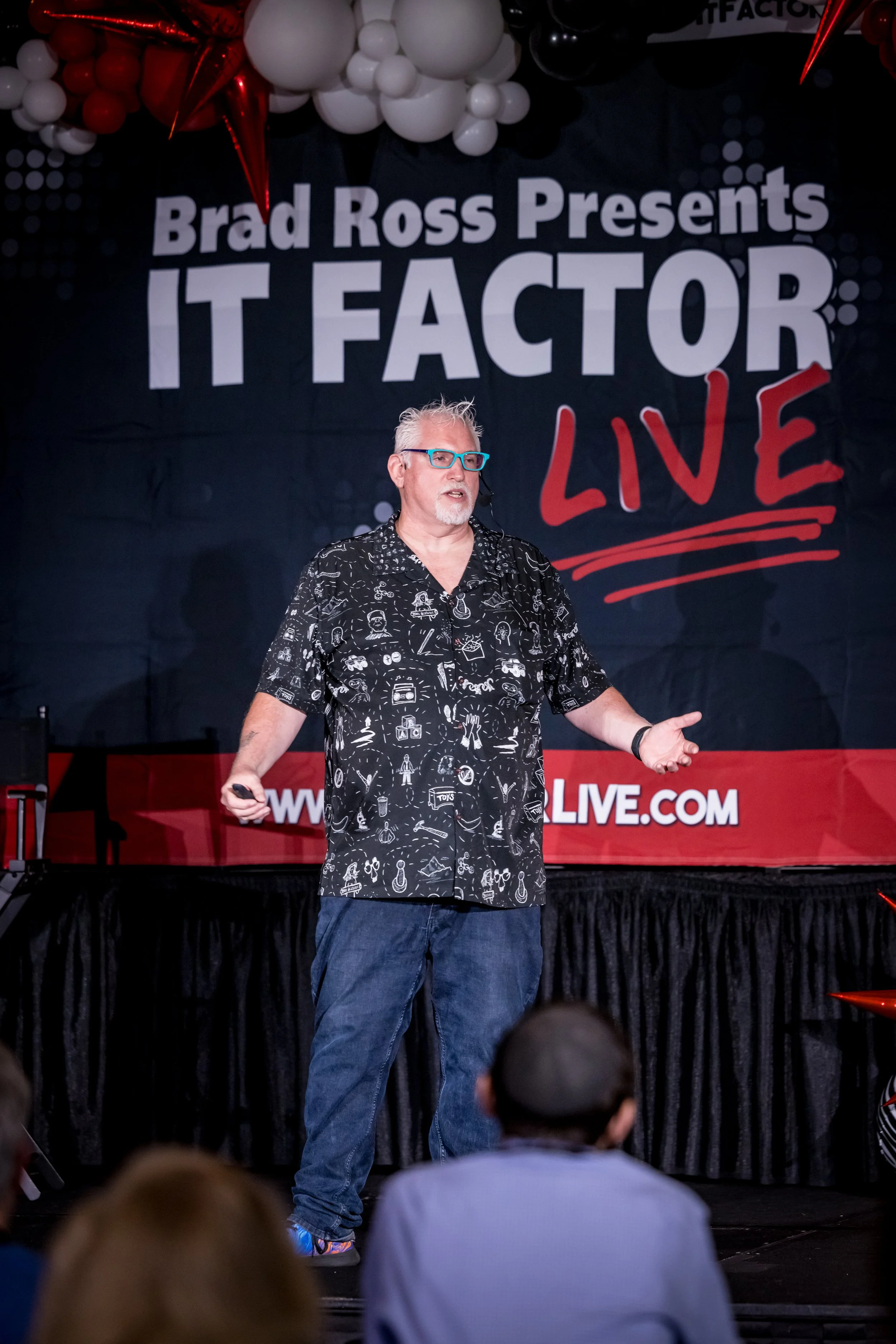 Mike Brennan speaking on stage at an event titled 'IT Factor Live'.
