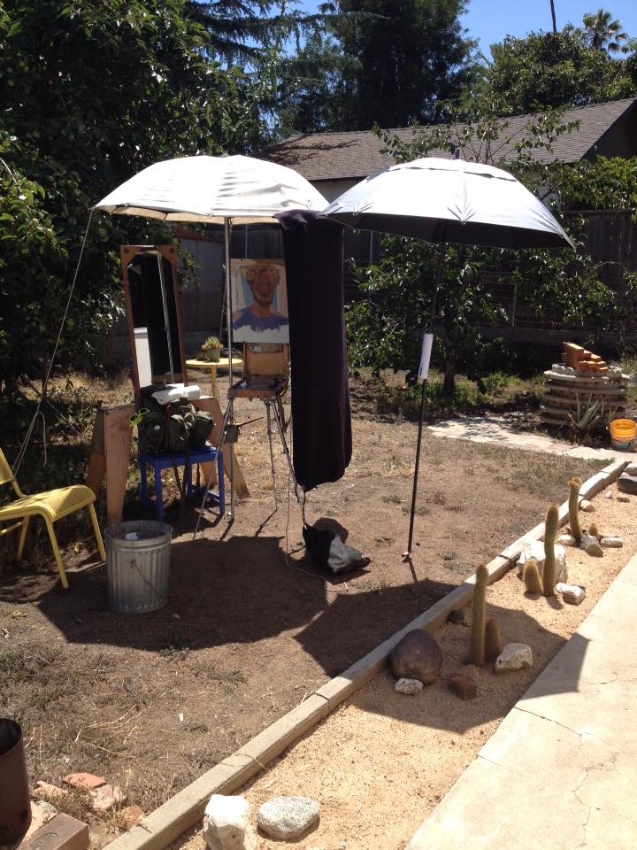 My setup: with a mirror just to the left of the easel, I had two umbrellas and a black fabric to help control reflected light.