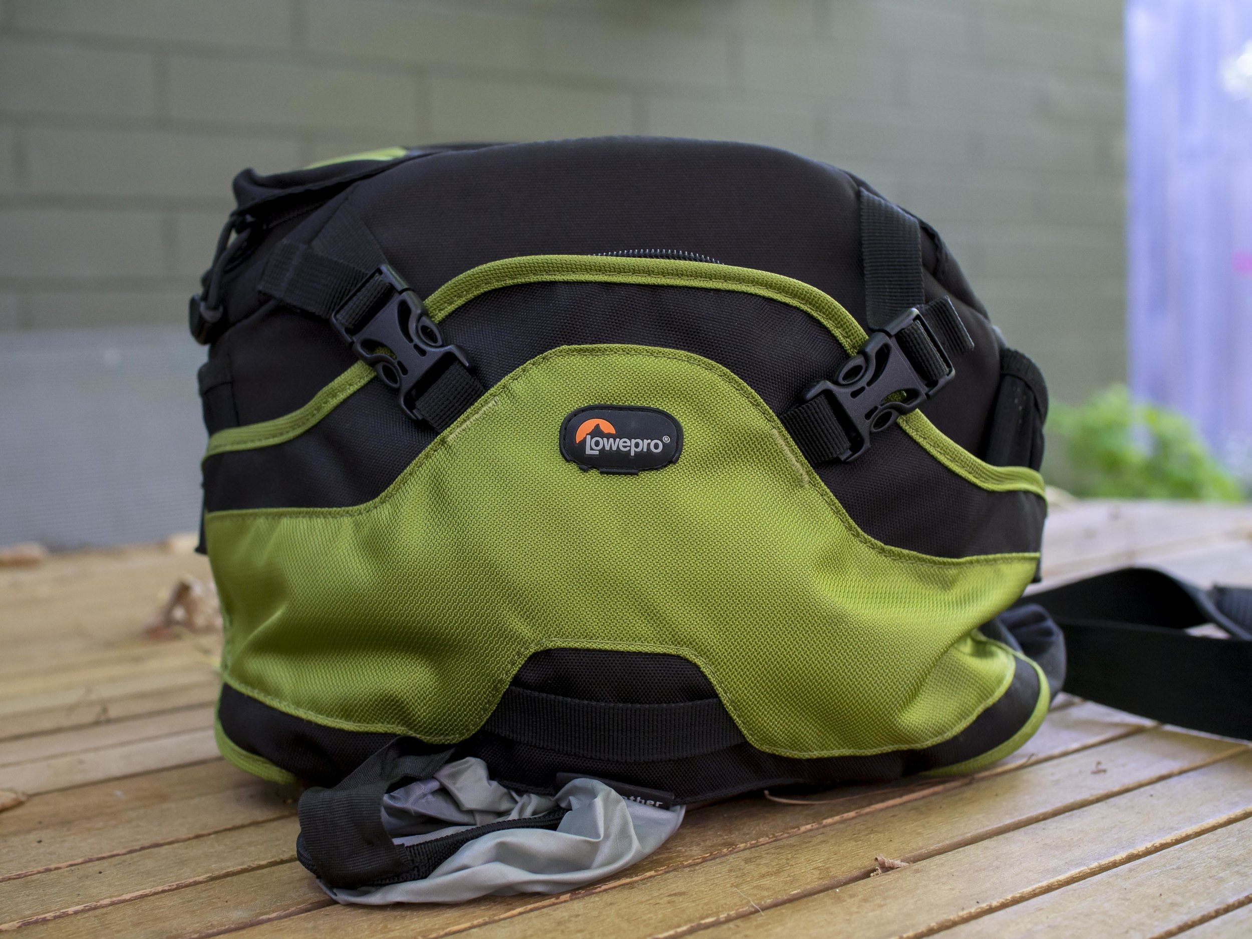 No, it’s not thirsty. The tongue hanging out is it’s weather shield cover. It also comes in basic black and a fetching Cobalt blue. Note no fanny pack wings, just bag. The clips at the front are the restraining straps for the front flap pocket. When pushed out fully the gap created can hold a camera body or lens while changing things out or expand the capacity of the front pocket. If the rain cover is removed, the pocket will hold even more as the two pockets occupy the same space.