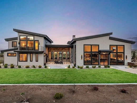 Modern two-story house with large windows, front lawn, and landscaped garden at sunset.