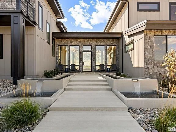 Front view of a modern house with steps leading to the entrance, surrounded by planters, on a partly cloudy day.