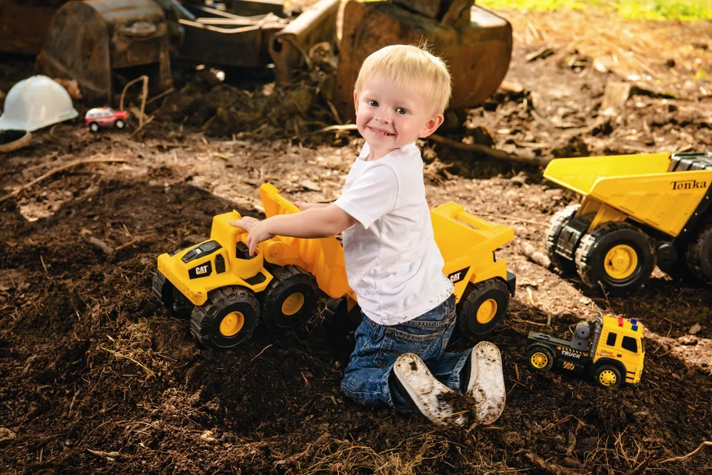 Child pushing a yellow toy dump truck through the dirt