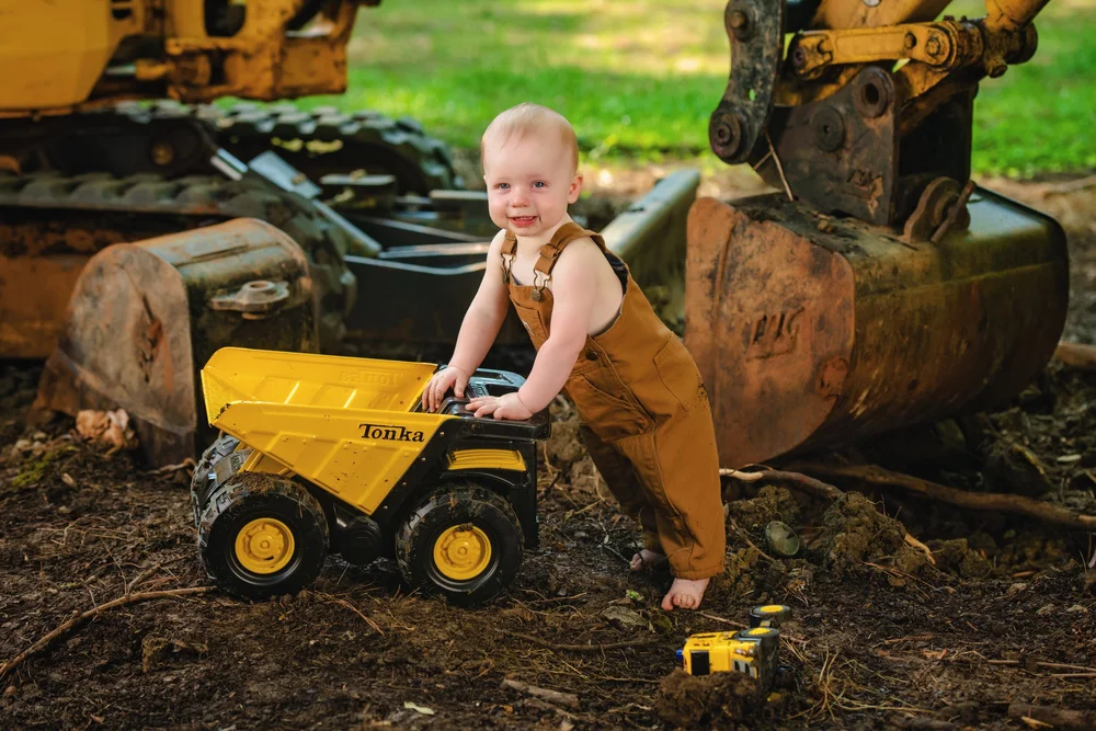 Toddler playing beside a real excavator and toy dump truck